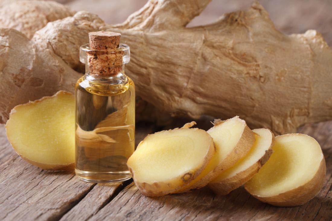 Ginger root sliced next to ginger essential oil in small bottle.