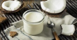 Coconut cut in half on tabletop with jar of coconut oil and spoon.