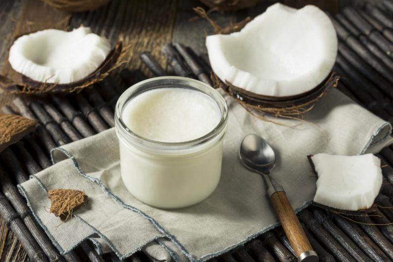 Coconut cut in half on tabletop with jar of coconut oil and spoon.