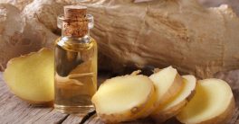 Ginger root sliced next to ginger essential oil in small bottle.